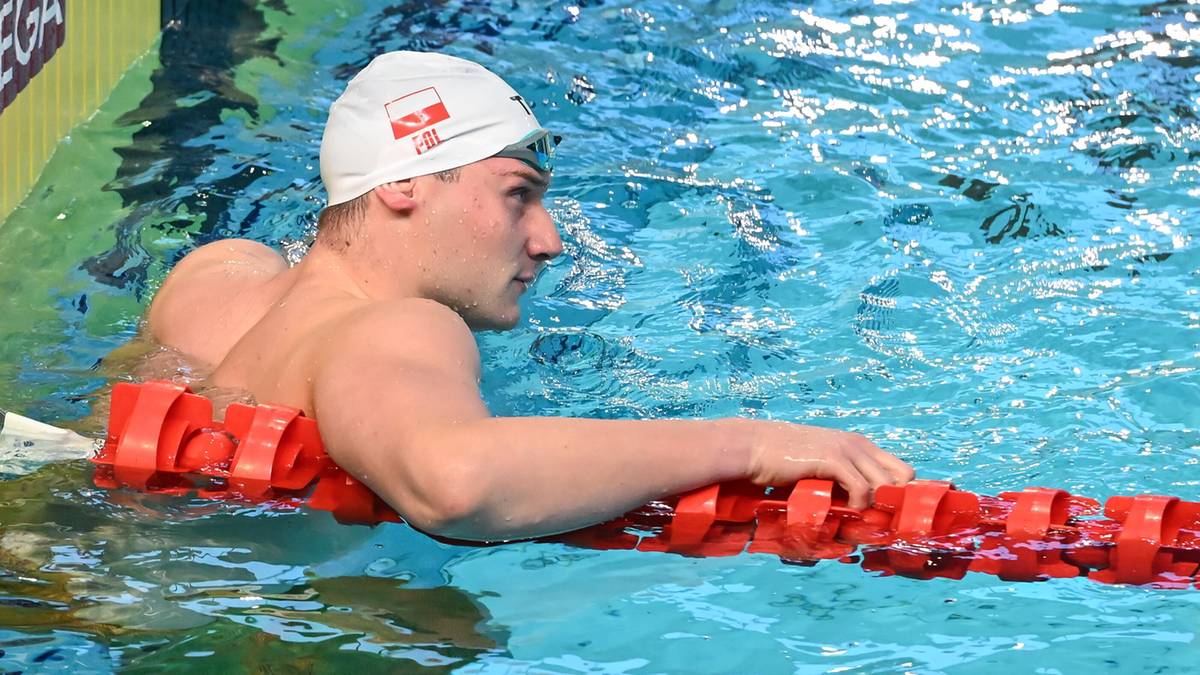 Pływak w czepku z polską flagą odpoczywa przy torze pływackim.