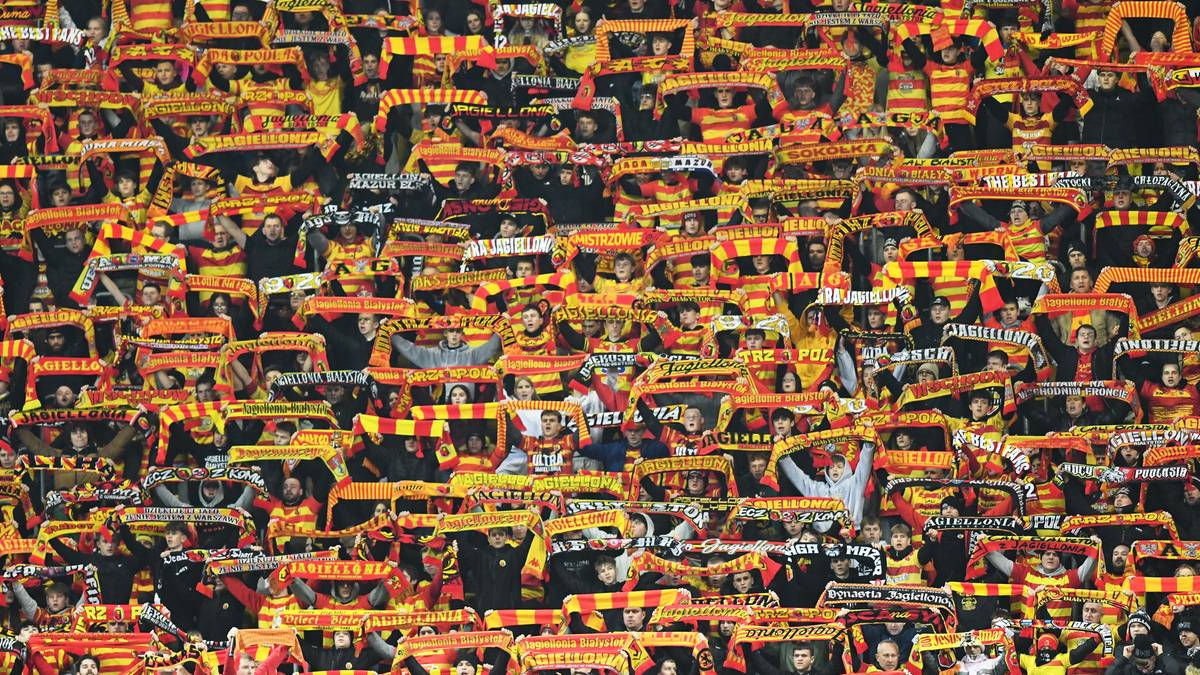 Tłum kibiców Jagiellonii Białystok trzymających szaliki w barwach klubu.