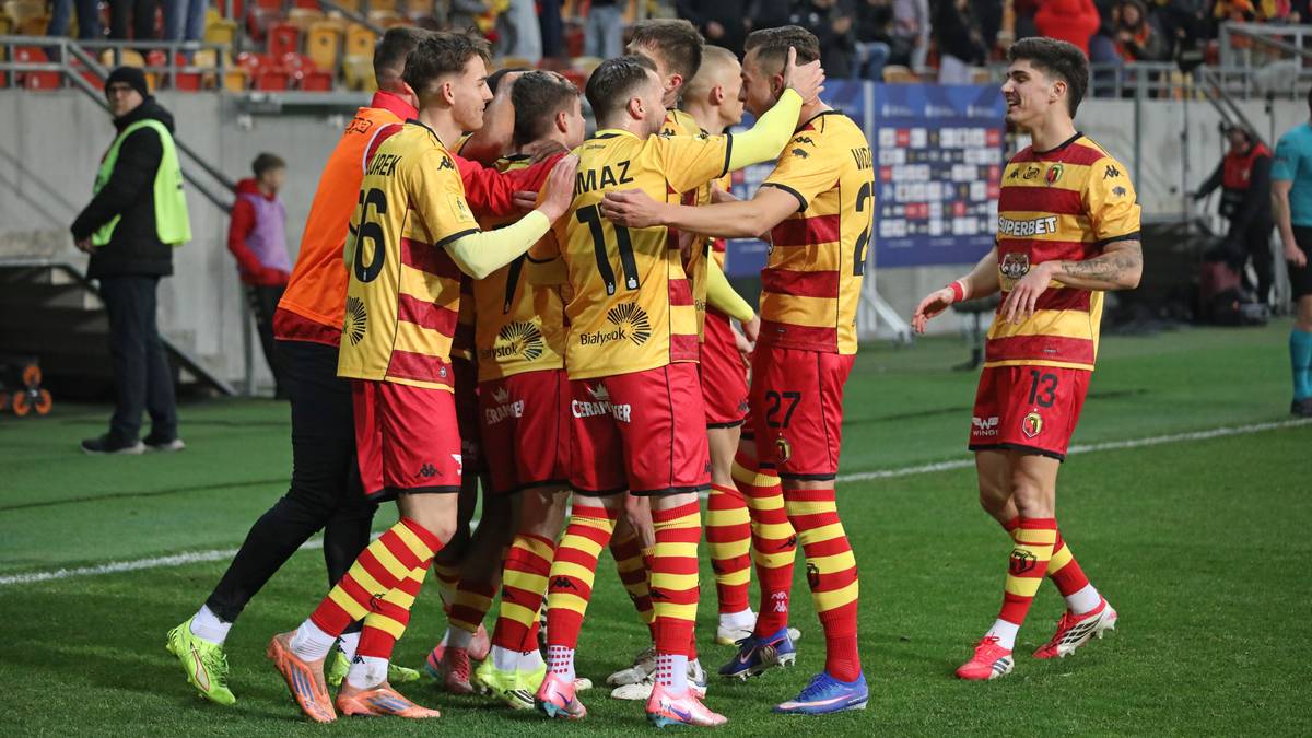 Piłkarze Jagiellonii Białystok w ż&oacute;łto-czerwonych strojach obejmują się, celebrując bramkę na boisku piłkarskim.
