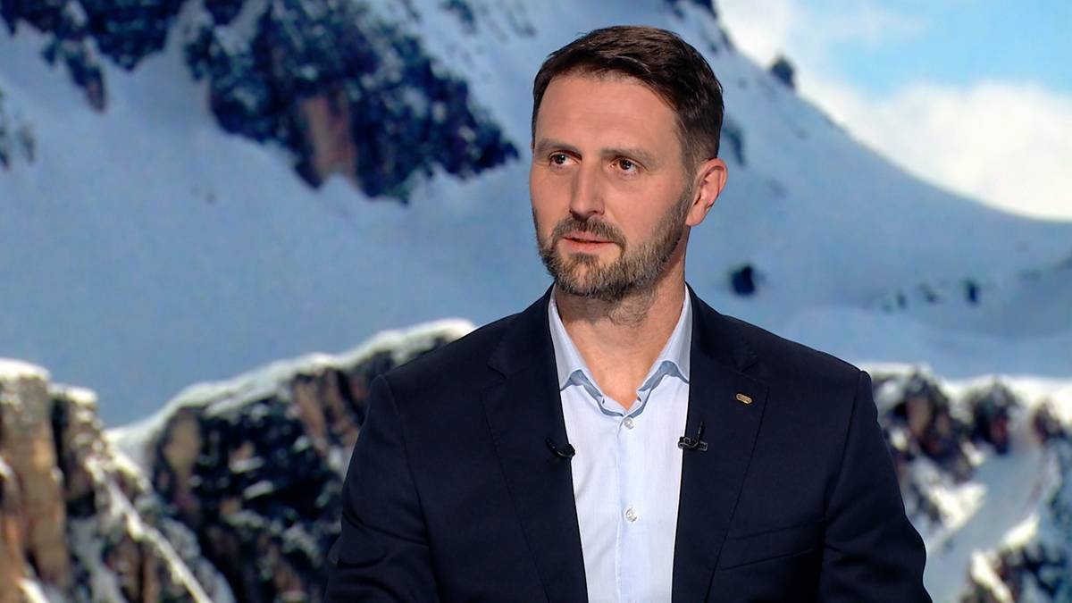 Mężczyzna w ciemnym garniturze i jasnej koszuli na tle zaśnieżonych gór.