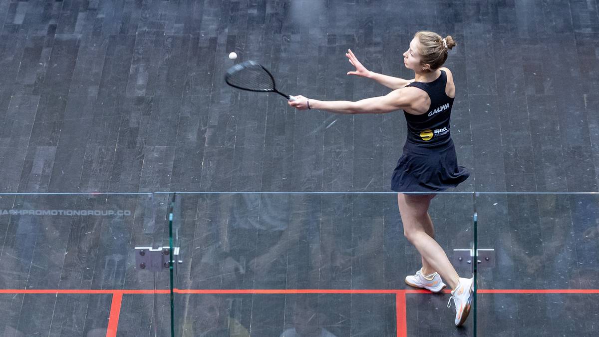 Kobieta grająca w squasha, odbija piłkę rakietą.