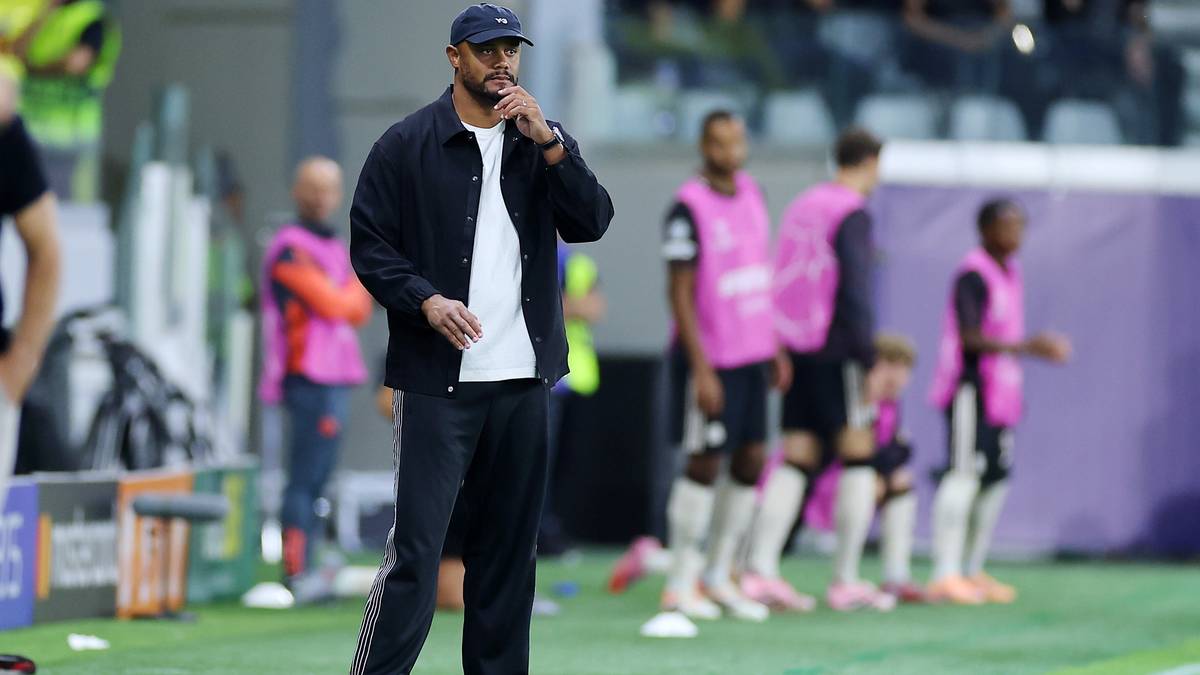 Trener Vincent Kompany w stroju sportowym stoi na boisku piłkarskim, obserwując mecz.