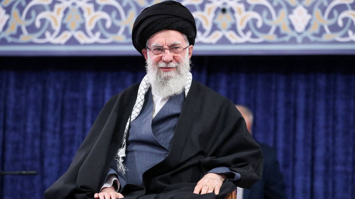 Portret Alego Chameneiego, najwyższego przyw&oacute;dcy Iranu, ubranego w tradycyjny str&oacute;j religijny i siedzącego na krześle.