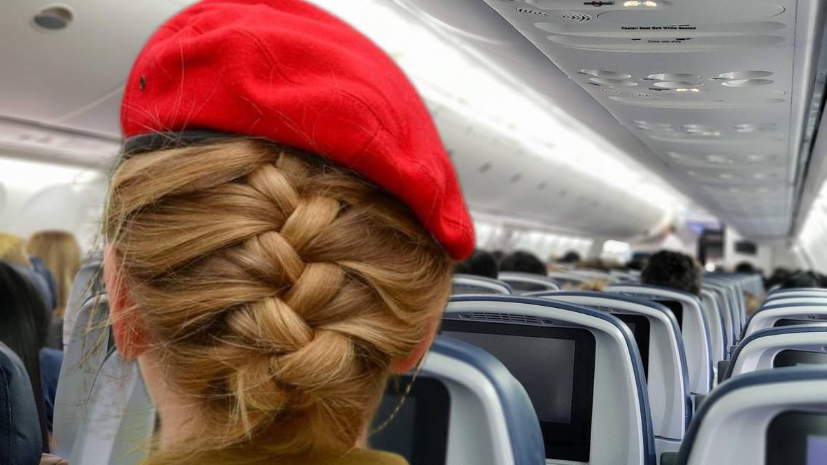 Widok zza plec&oacute;w kobiety w czerwonym berencie, siedzącej w samolocie. Widoczne jej splecione włosy, a także rzędy siedzeń i okna samolotu.