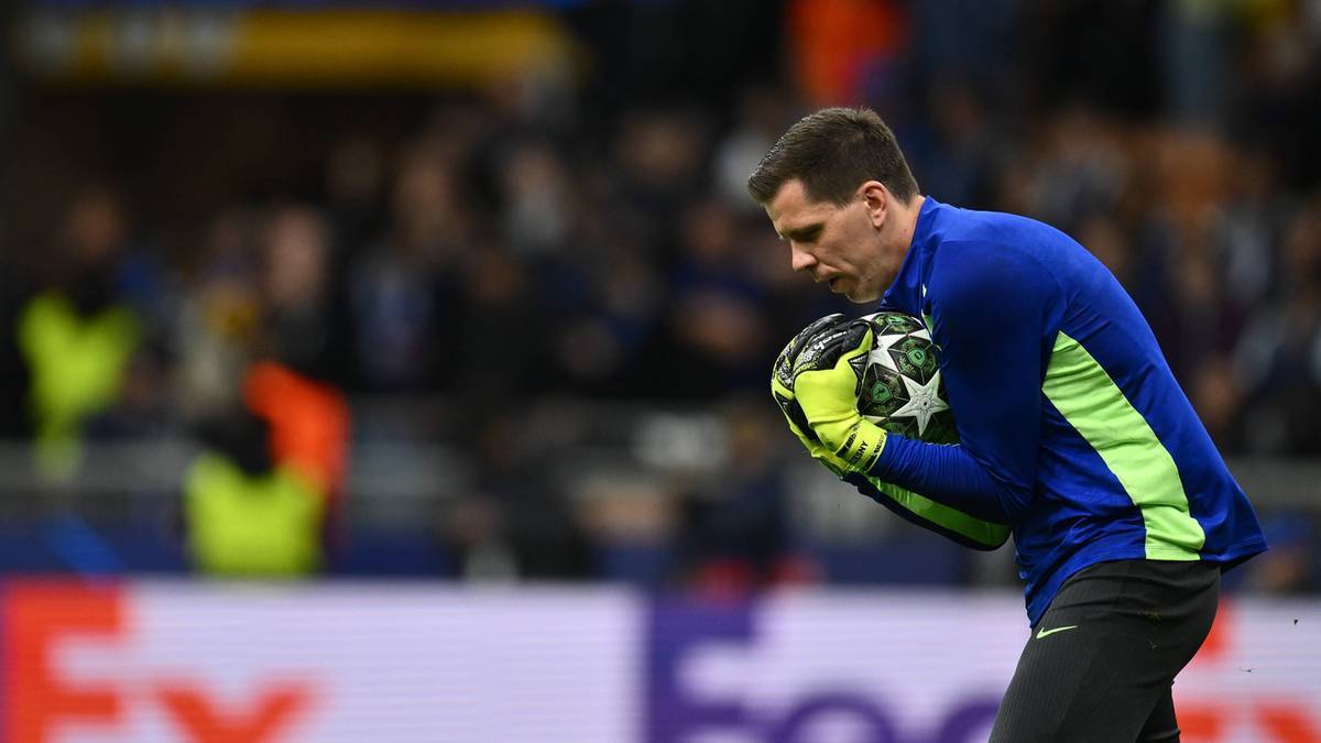 Bramkarz Wojciech Szczęsny w niebieskiej koszulce z zielonymi wstawkami trzyma piłkę nożną w rękawicach, skupiony na grze.