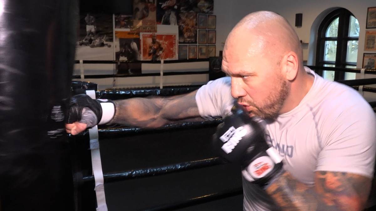 Mężczyzna w rękawicach bokserskich ćwiczy na worku treningowym w ringu.