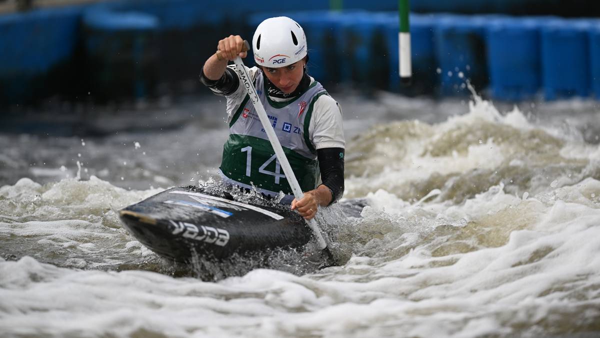 Sportowiec w białym kasku płynący kajakiem przez wzburzoną wodę na torze slalomowym.