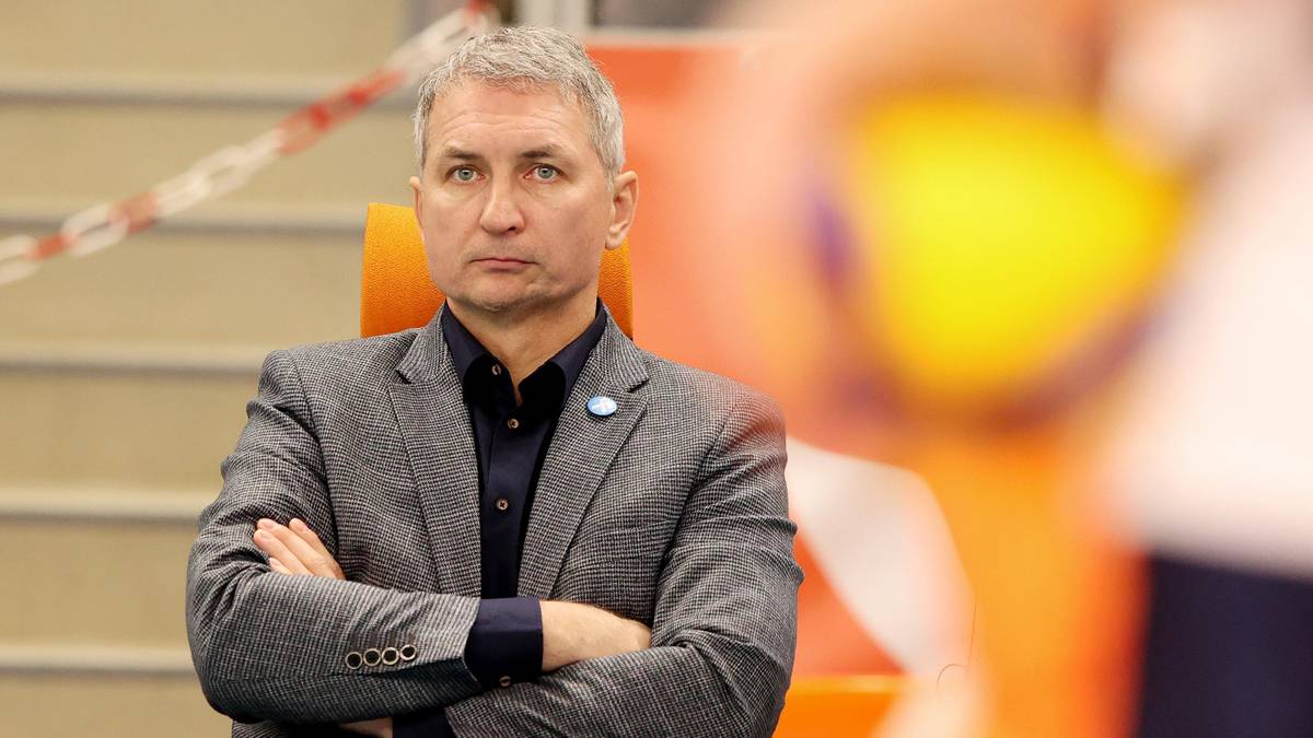 Mężczyzna w garniturze siedzi ze skrzyżowanymi rękami, patrząc przed siebie.