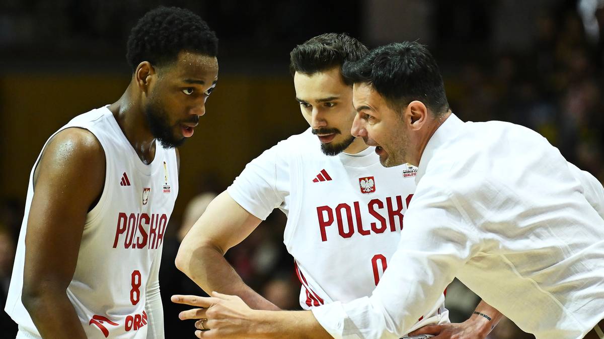 Trzech mężczyzn w strojach sportowych podczas rozmowy na boisku koszykarskim.