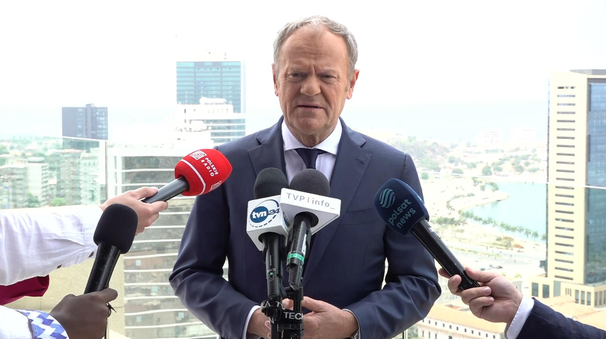 Premier Donald Tusk przemawia do dziennikarzy, trzymając ręce lekko rozłożone.