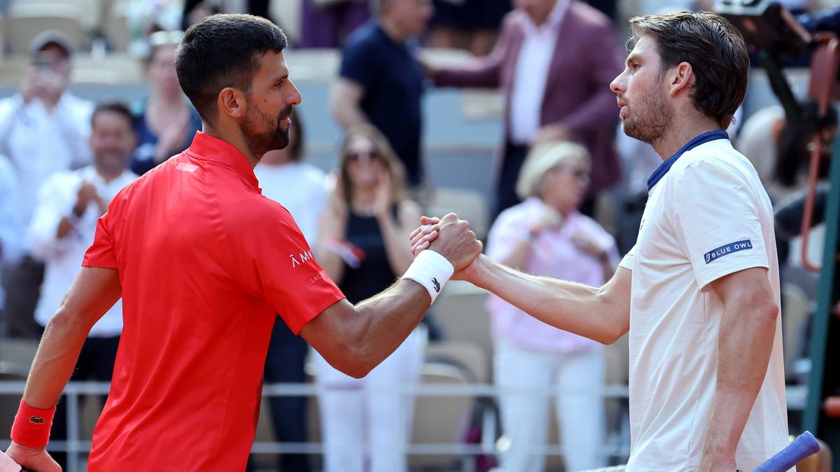 Novak Djoković w czerwonej koszulce i jego przeciwnik w białej koszulce ściskają sobie ręce na korcie tenisowym po meczu.