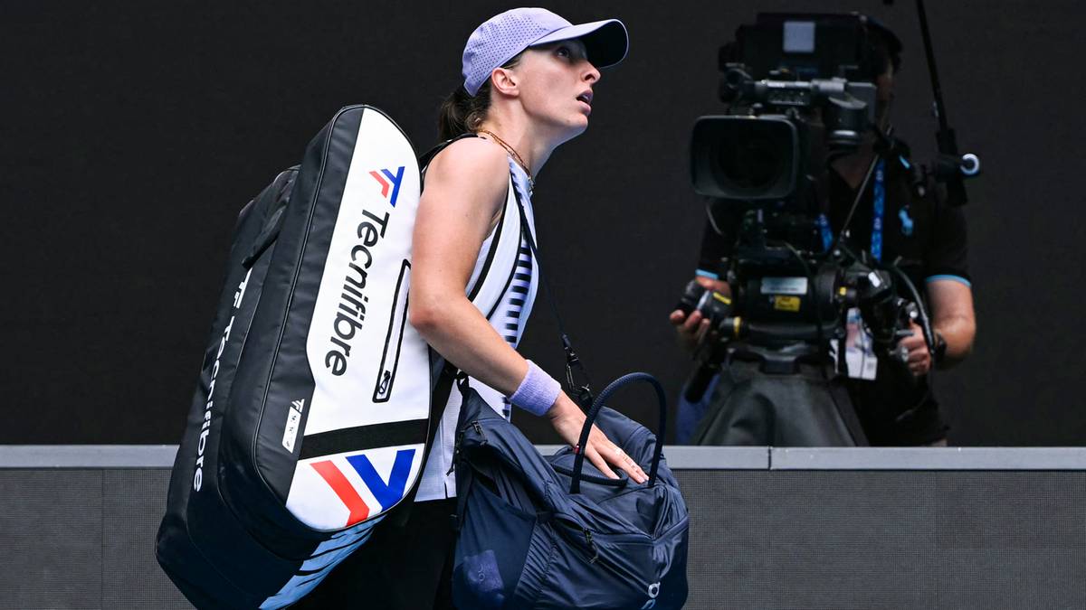 Tenisistka w czapce i stroju sportowym z torbą na ramieniu idzie obok kamery telewizyjnej.