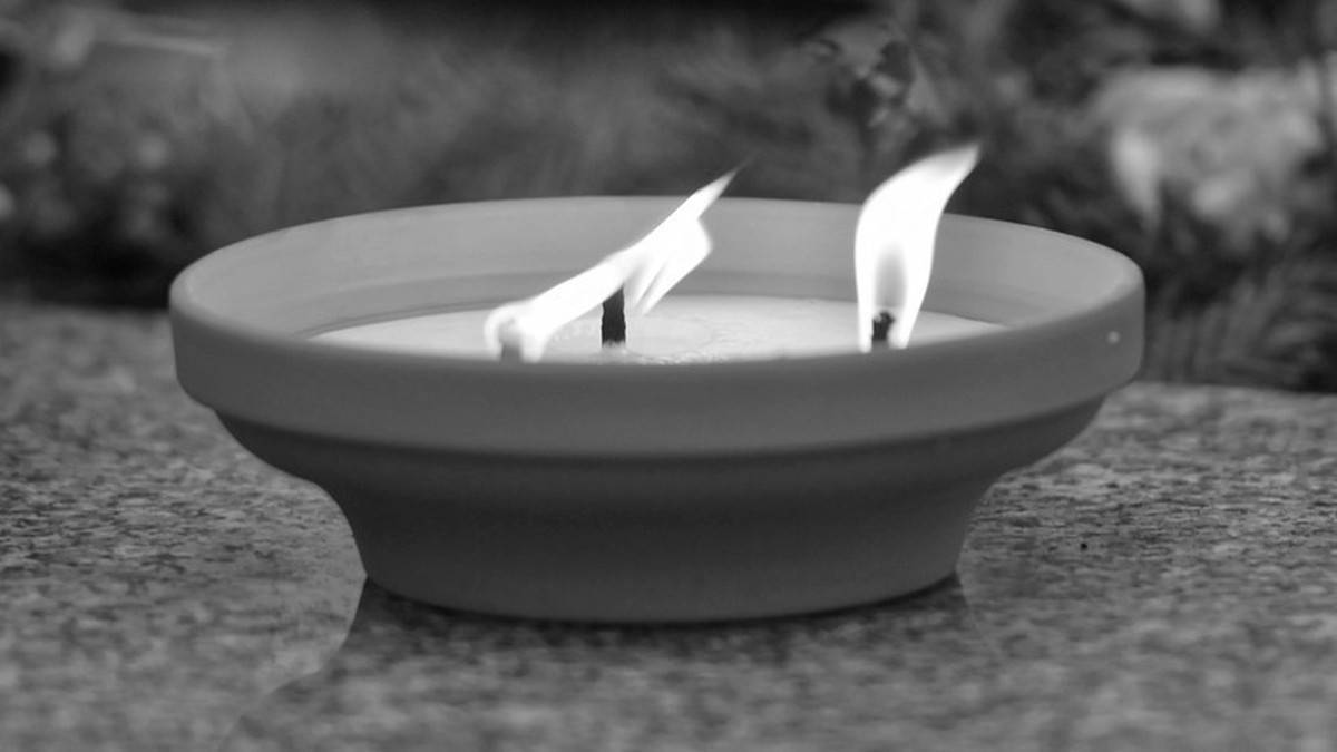 Dwa płonące znicze na nagrobku.