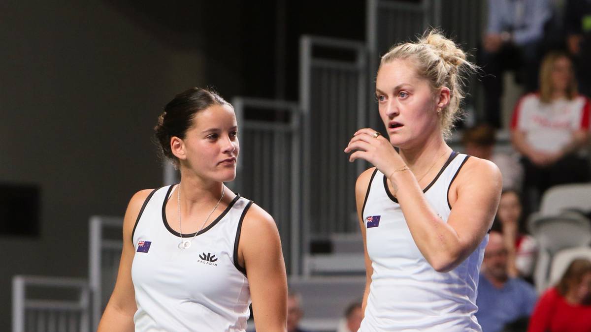 Dwie tenisistki w białych strojach sportowych na korcie tenisowym, patrzące w różne strony.