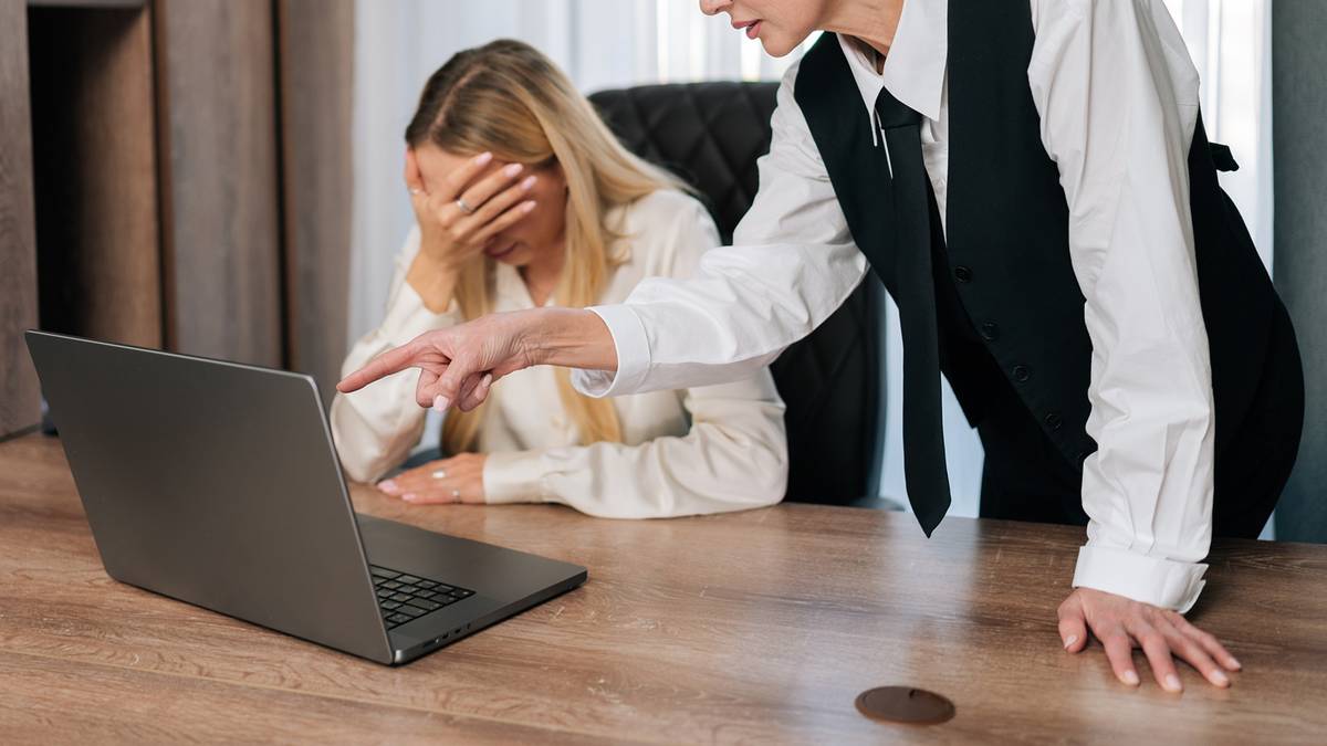 Kobieta zestresowana przy laptopie, druga kobieta wskazuje na ekran