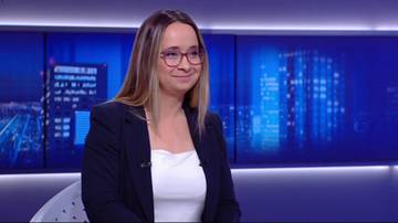 Kobieta w okularach i ciemnym żakiecie siedzi w studiu telewizyjnym.