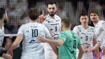 Siatkarze PGE Projekt Warszawa w białych strojach podczas meczu, jeden z zawodnik&oacute;w pokazuje palcem w g&oacute;rę.
