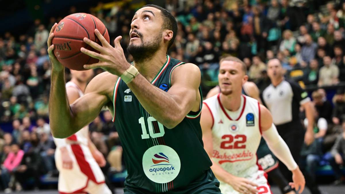Koszykarz z numerem 10 na zielonym stroju przygotowuje się do rzutu, trzymając piłkę obiema rękami.
