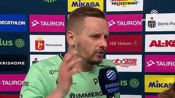 Damian Wojtaszek, mężczyzna z kr&oacute;tkimi blond włosami i zarostem, ubrany w zieloną koszulkę, m&oacute;wi do mikrofonu na tle ścian z kolorowymi banerami sponsor&oacute;w.