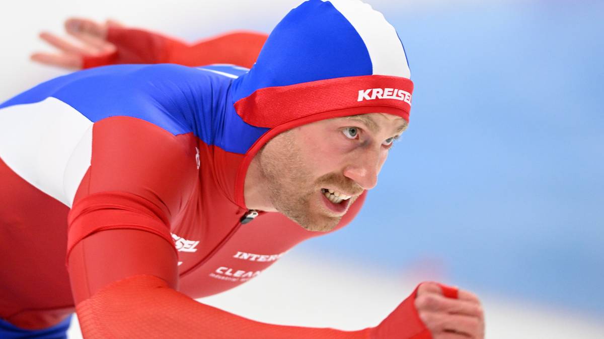 Łyżwiarz szybki w czerwono-niebieskim stroju, zdeterminowany wyraz twarzy.