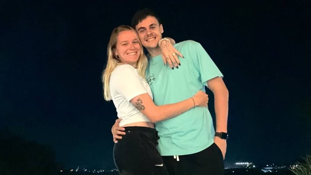 Para młodych ludzi, kobieta i mężczyzna, uśmiechają się do kamery. Kobieta jest uściskana przez mężczyznę, który obejmuje ją w pasie. Oboje są ubrani w sportowe ubrania.