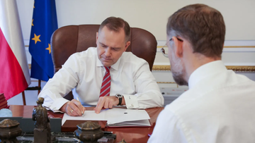 Minister obrony narodowej Władysław Kosiniak-Kamysz siedzi przy biurku i podpisuje dokumenty, podczas gdy drugi mężczyzna obserwuje.