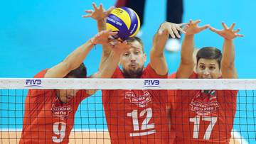 Siatkarze w czerwonych strojach walczą o piłkę nad siatką.