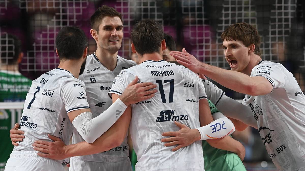 Grupa siatkarzy w białych strojach, świętujących razem na boisku.