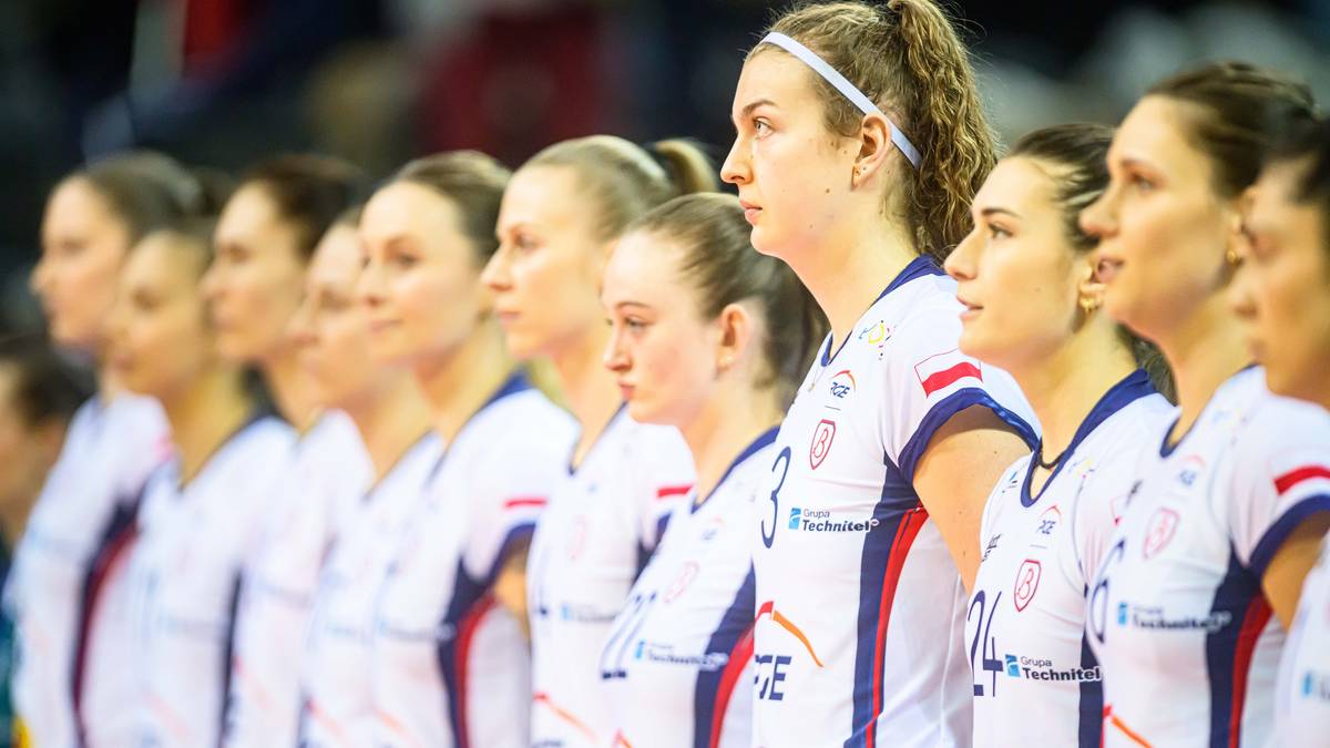 Grupa siatkarek w białych strojach sportowych stoi obok siebie.