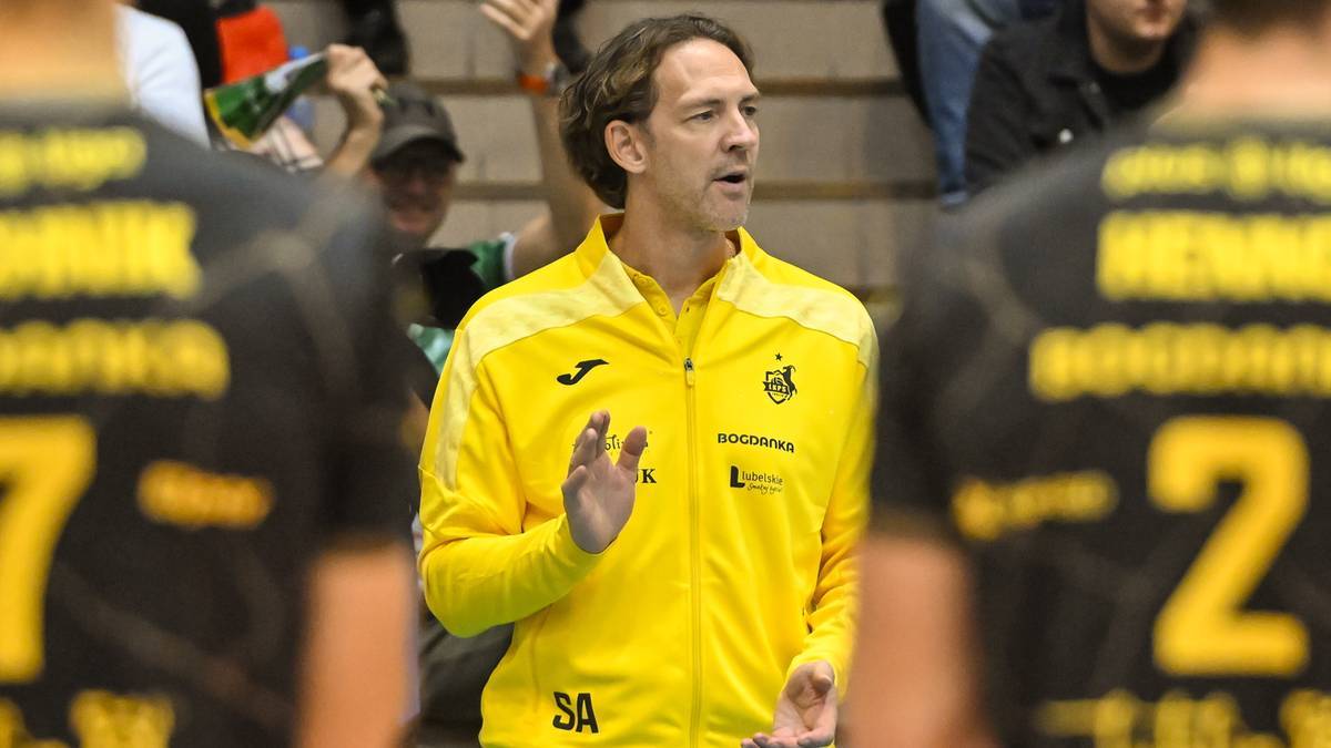 Trener w ż&oacute;łtej bluzie sportowej gestykuluje podczas meczu siatk&oacute;wki.