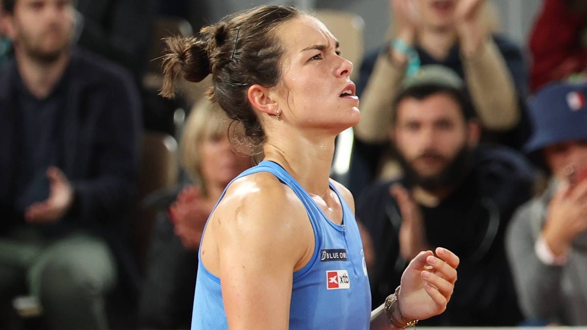 Tenisistka Lois Boisson w akcji, skupiona, w niebieskiej koszulce, z włosami upiętymi w kok.