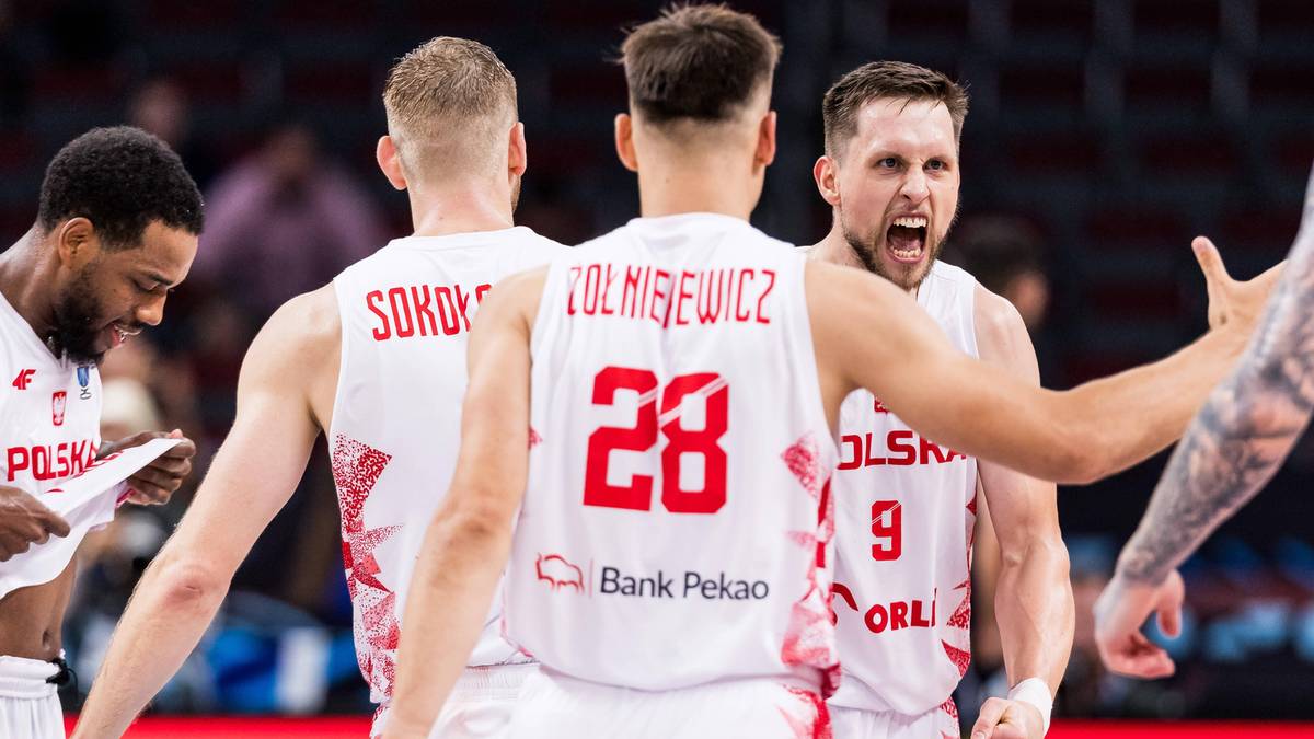 Fragment meczu koszykówki, zawodnicy reprezentacji Polski w białych koszulkach z numerami.