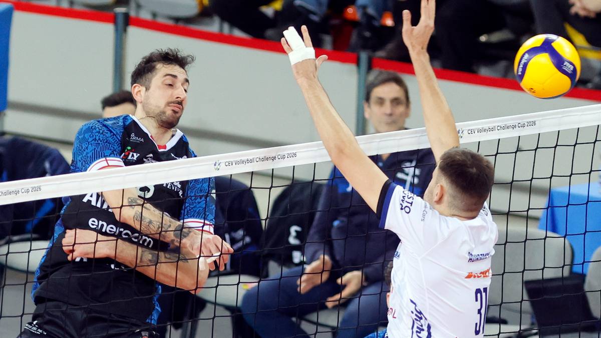 Siatkarze podczas meczu siatk&oacute;wki, jeden z nich wykonuje zagrywkę, a drugi blokuje.