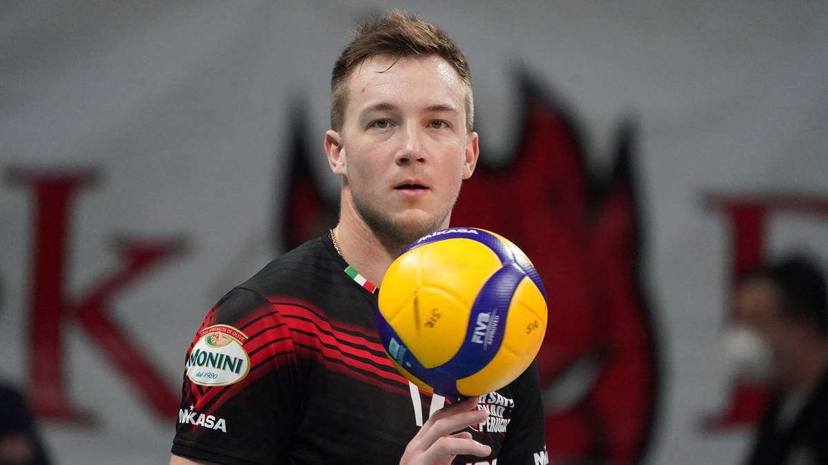 Siatkarz w czarnej koszulce z czerwonymi pasami trzymający piłkę do siatk&oacute;wki.