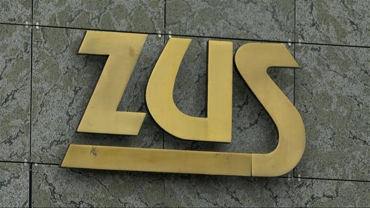 Złote logo ZUS na szarej, kafelkowej ścianie.
