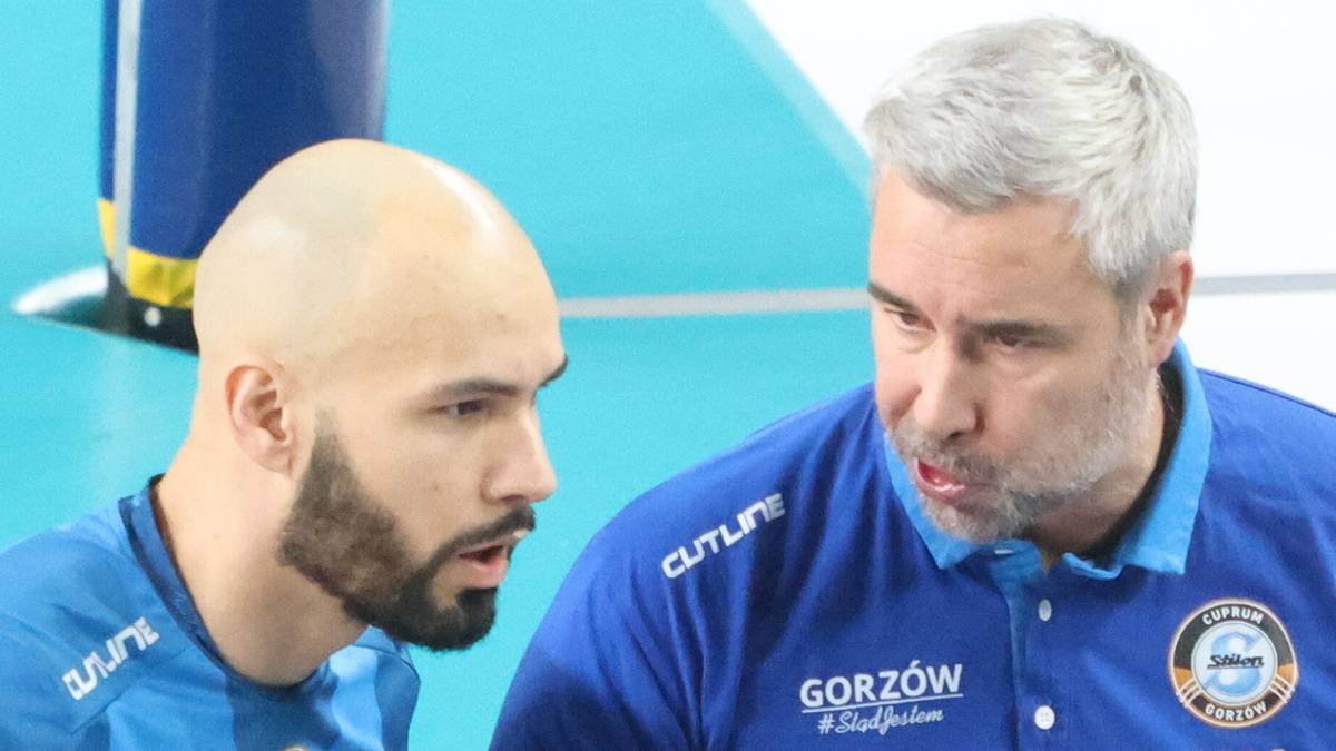 Dw&oacute;ch mężczyzn w niebieskich strojach sportowych dyskutuje na boisku.