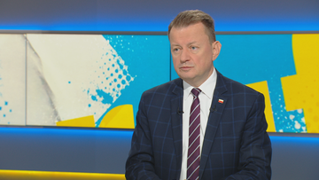 Mężczyzna w garniturze siedzi przed ekranem z abstrakcyjnym wzorem.