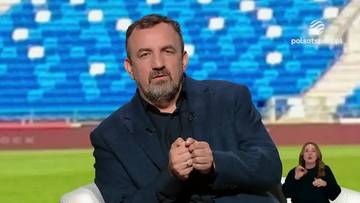 Mariusz Misiura w ciemnej marynarce siedzi przed widownią stadionu piłkarskiego, zamyślony, z dłońmi złożonymi na piersi.