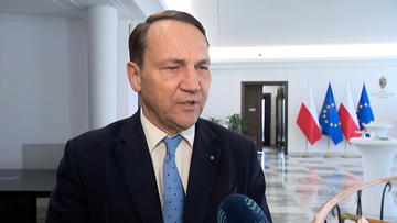 Mężczyzna w garniturze i krawacie udziela wywiadu, w tle widoczne są flagi Polski i Unii Europejskiej.