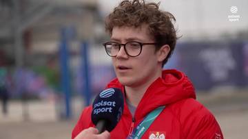 Mężczyzna w okularach i czerwonej kurtce z kapturem odpowiada na pytanie dziennikarza, trzymając mikrofon Polsat Sport.