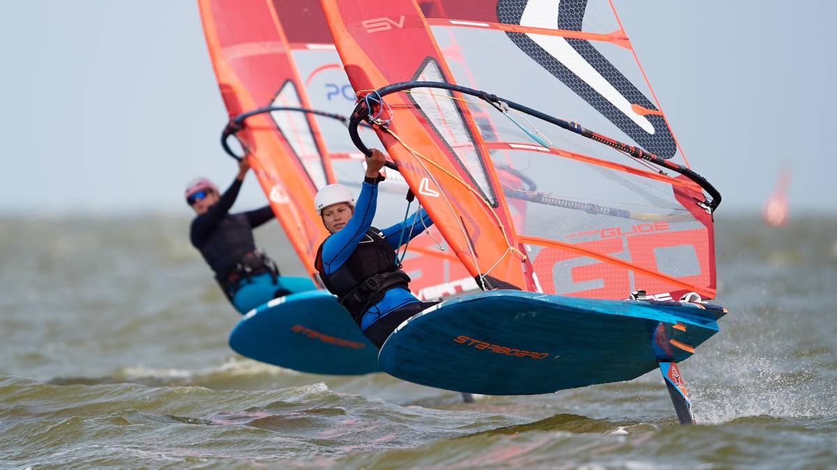 Dw&oacute;ch zawodnik&oacute;w na deskach windsurfingowych z żaglami ścigających się na wodzie.