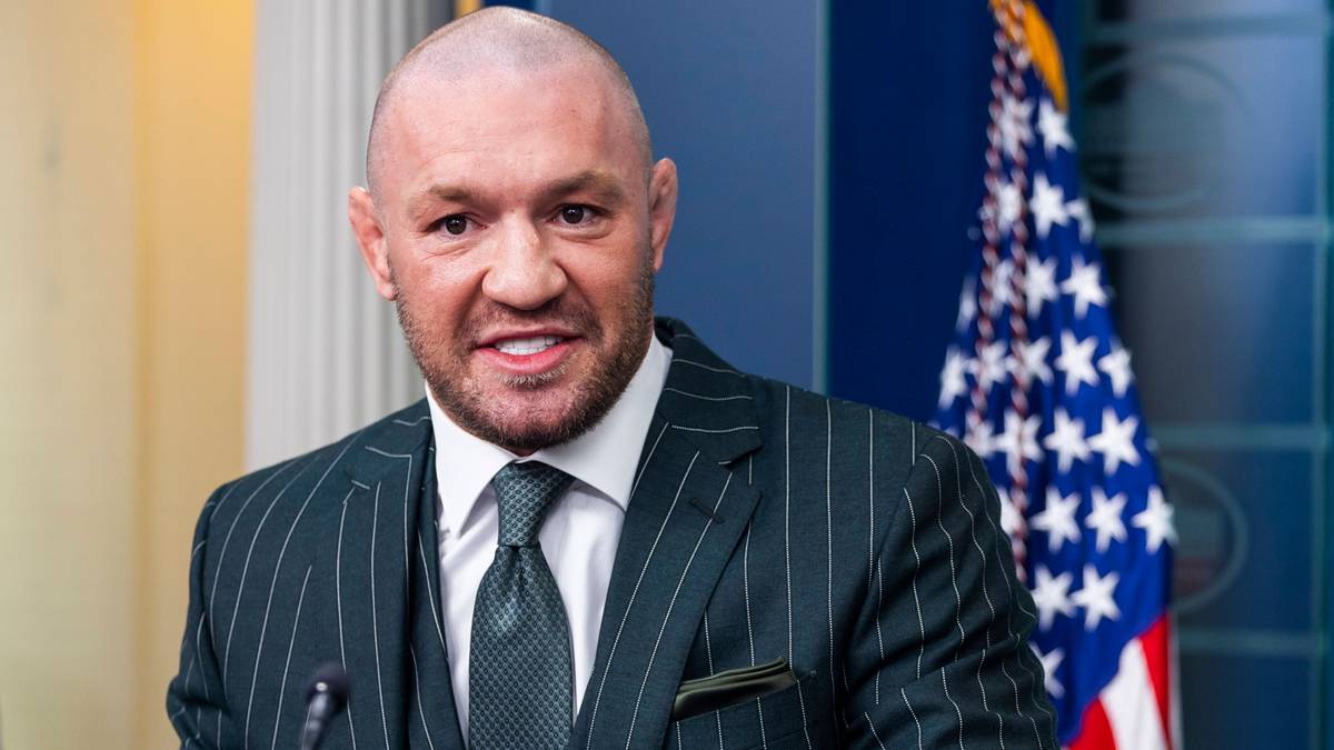 Portret Conora McGregora w garniturze stojącego przed flagą amerykańską.