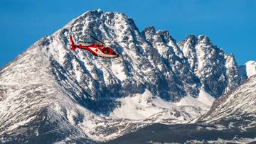 Czerwono-biały helikopter ratowniczy latający na tle ośnieżonych g&oacute;r.