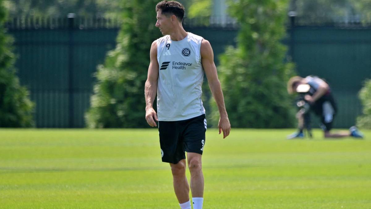 Piłkarz Robert Lewandowski w białej koszulce i czarnych spodenkach na boisku piłkarskim.