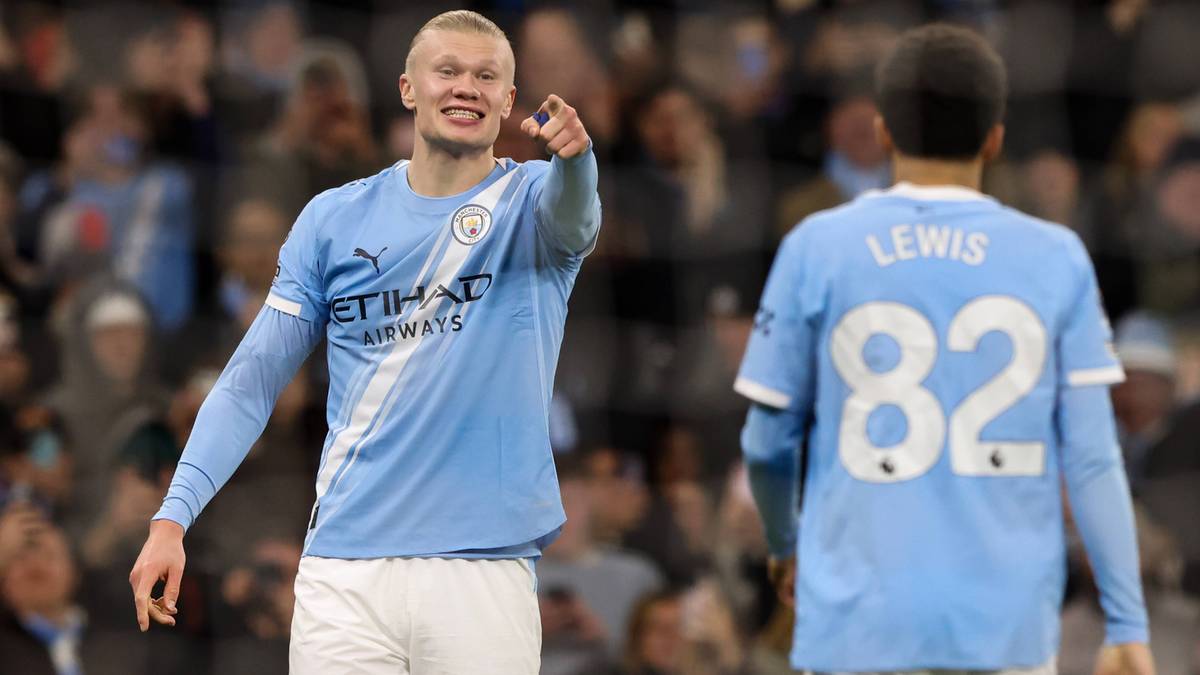 Piłkarz Manchesteru City Erling Haaland uśmiecha się i wskazuje palcem w stronę widza, obok niego stoi inny piłkarz.