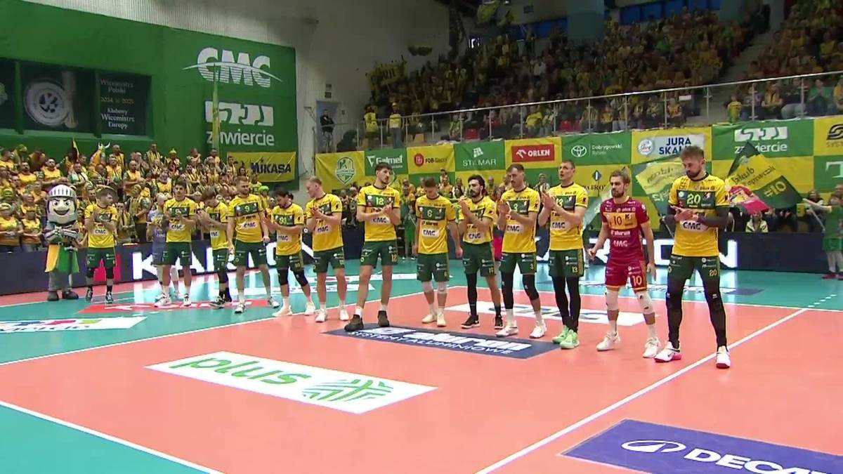 Siatkarze Aluronu CMC Warta Zawiercie w żółtych strojach stoją w szeregu na boisku, przed publicznością.
