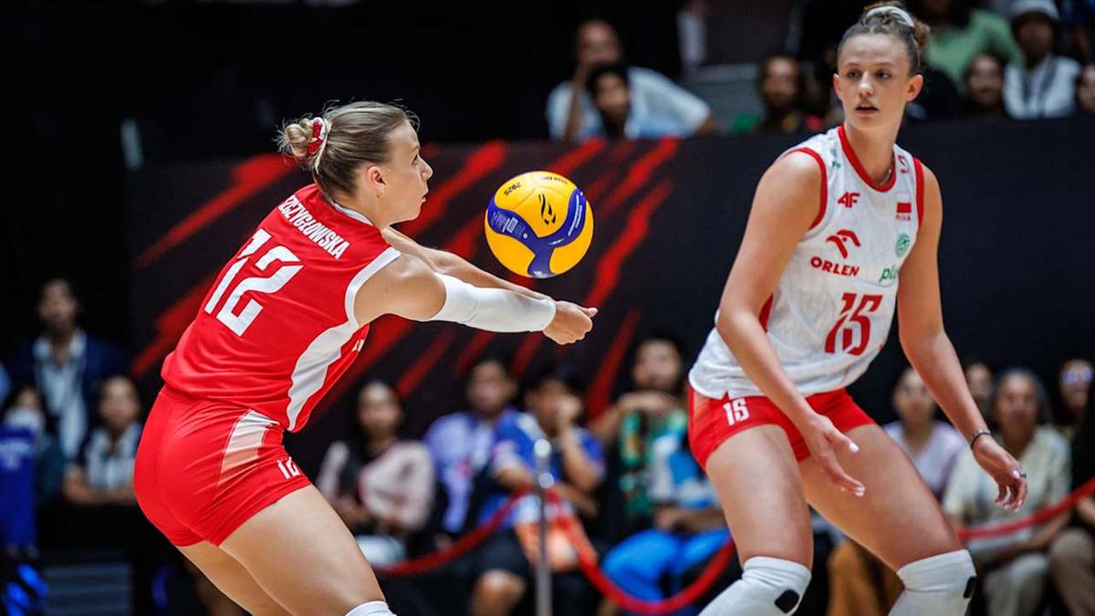 Dwie siatkarki w białych i czerwonych strojach rywalizują podczas meczu. Jedna z nich, w czerwonej bluzce z numerem 12, odbija piłkę.