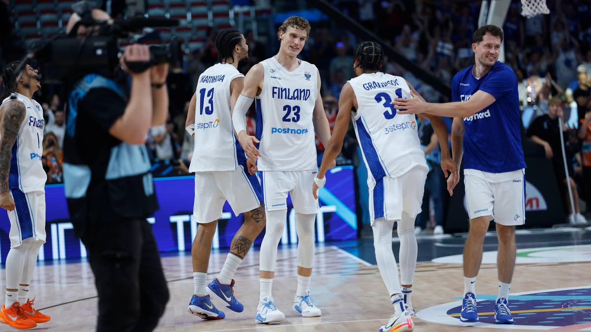 Drużyna Finlandii w białych strojach meczowych z numerami na plecach, cieszy się po zwycięstwie na boisku do koszykówki. Widoczni zawodnicy, trener i kamera.