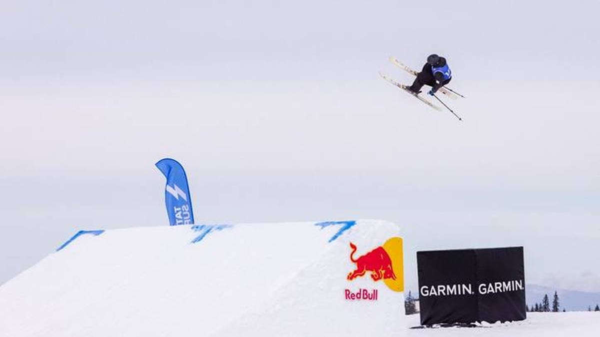 Narciarz wykonujący skok w powietrzu nad śnieżną rampą podczas zawod&oacute;w.