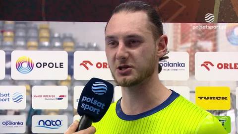 Krzysztof Komarzewski udziela wywiadu z mikrofonem w ręku, na tle ścianki z logotypami sponsor&oacute;w.